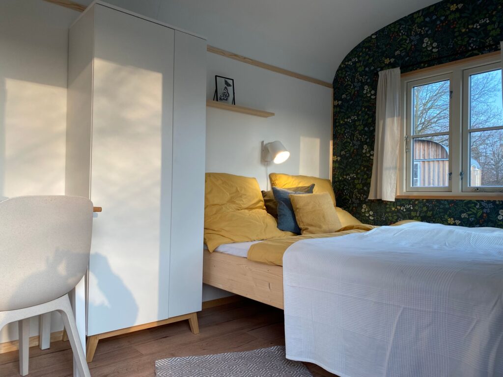 Gemütlicher Schlafbereich mit Bett, Schrank und Fenster im Bauwagen.