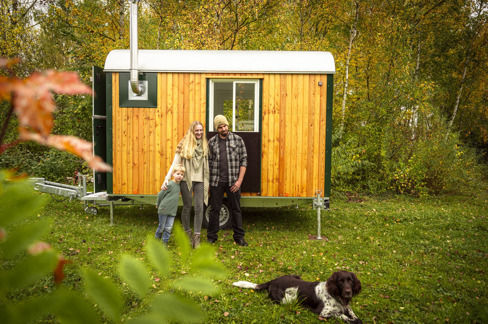 Familie mit Hund steht in der Natur vor dem Bauwagen
